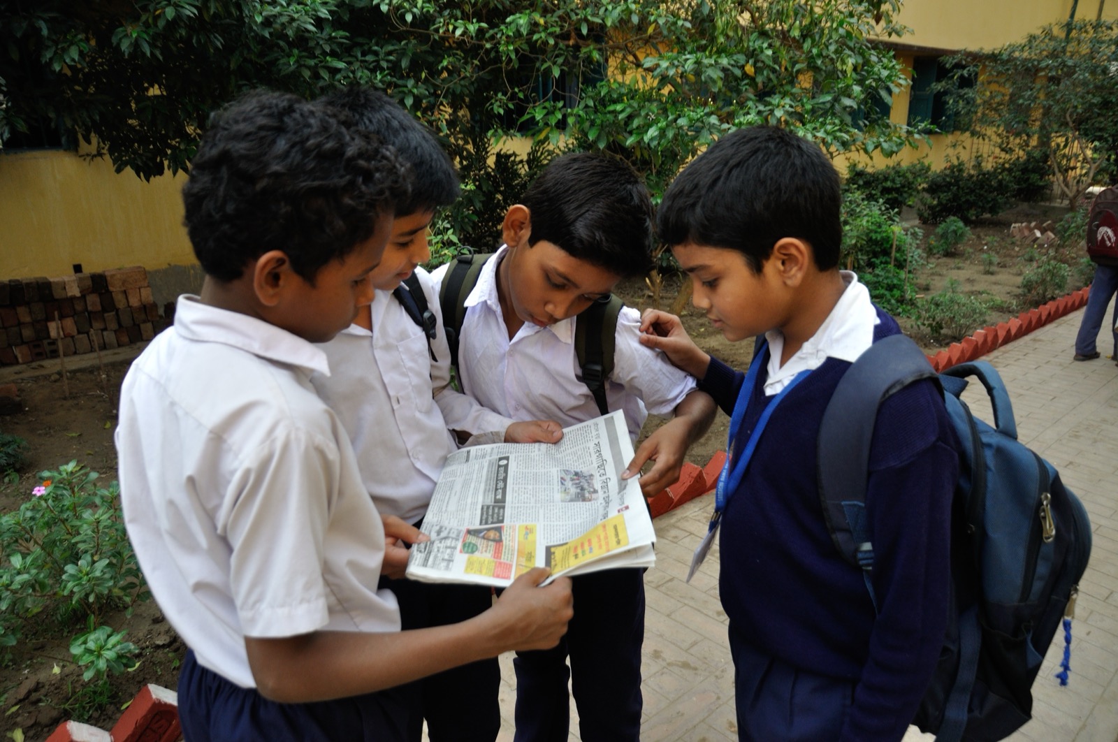 A group of students sitting together and reading a newspaper spread open between them